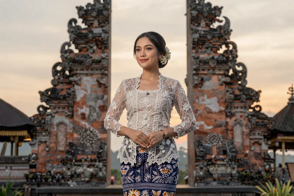 Indonesian woman in elegant attire with traditional Balinese temple backdrop at sunset